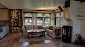 A cozy living room with a stone wall, a fireplace, and large windows offering a view of the outdoors. - Hulder- og Trollparken (Senja)