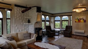 A spacious living room with a fireplace, comfortable seating, and large windows offering a view of the outdoors. - Hulder- og Trollparken (Senja)