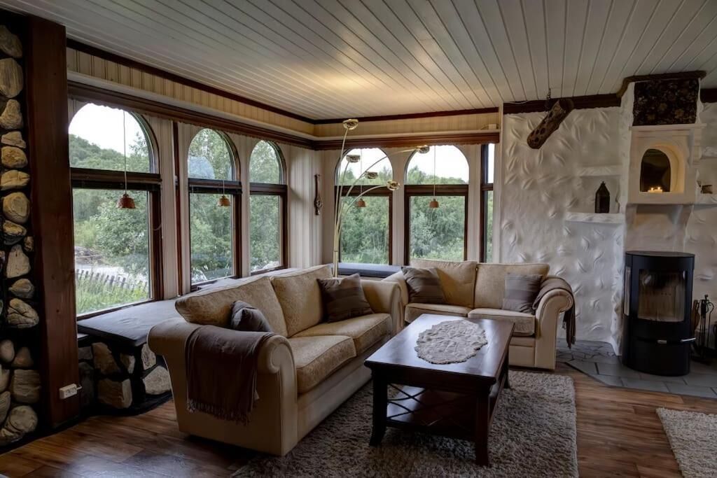 A cozy living room with a stone wall, a fireplace, and a large window overlooking greenery.