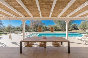 A covered outdoor dining area with a pool in the background. - 4201 Terrazze Ai Demani by Perle di Puglia (Manduria)
