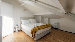 Ein Schlafzimmer mit schrägen Wänden, einem Bett mit weißer Bettwäsche, einem kleinen Nachttisch und einem Heizgerät.