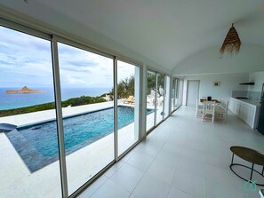 A modern interior with a large glass wall overlooking a swimming pool and ocean view. - Padel Resort Villa Olivier (Raf Raf)