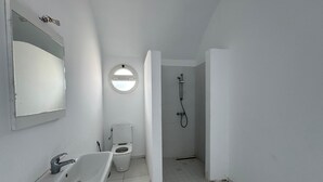 Un baño pequeño y blanco con lavamanos, inodoro y ducha.