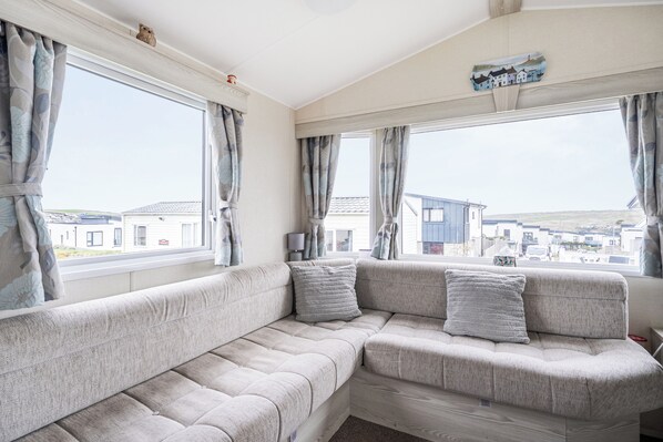 Una sala de estar acogedora con un sofá modular, ventanas amplias y vistas del entorno.