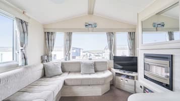 A caravan interior with a sofa, television, and a view of houses through the windows.
