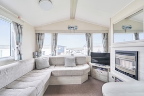 A caravan interior with a sofa, television, and a view of houses through the windows. - Perranporthcaravan/2bedroom/tv/gasfire (Perranporth)