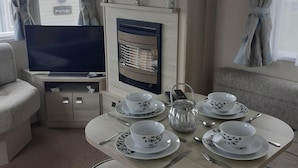 Ein gemütlicher Wohnbereich mit Fernseher, Kamin und Essplatz mit Tee-Sets.