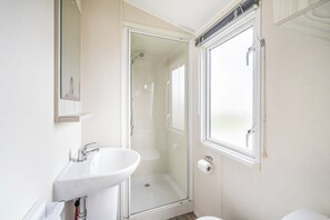 Un baño con cabina de ducha de vidrio, un lavabo blanco y un inodoro.