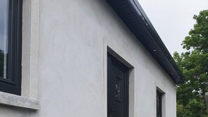 Un edificio con una escalera de piedra que conduce a una puerta, una mesa pequeña con sillas y una ventana.