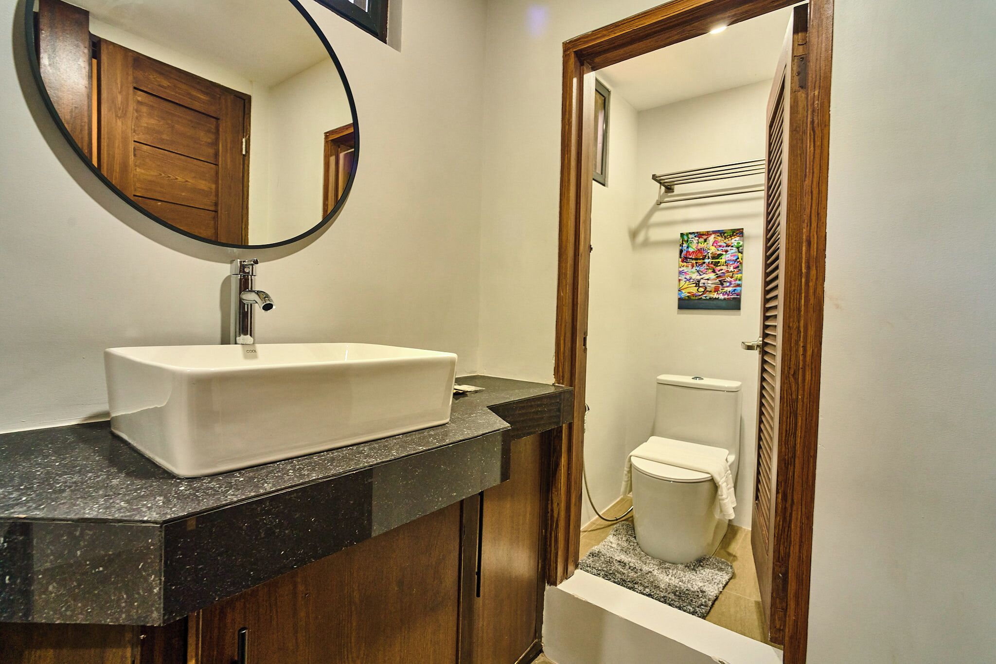 A bathroom with a white sink, a wooden door, and a toilet visible through an open doorway.