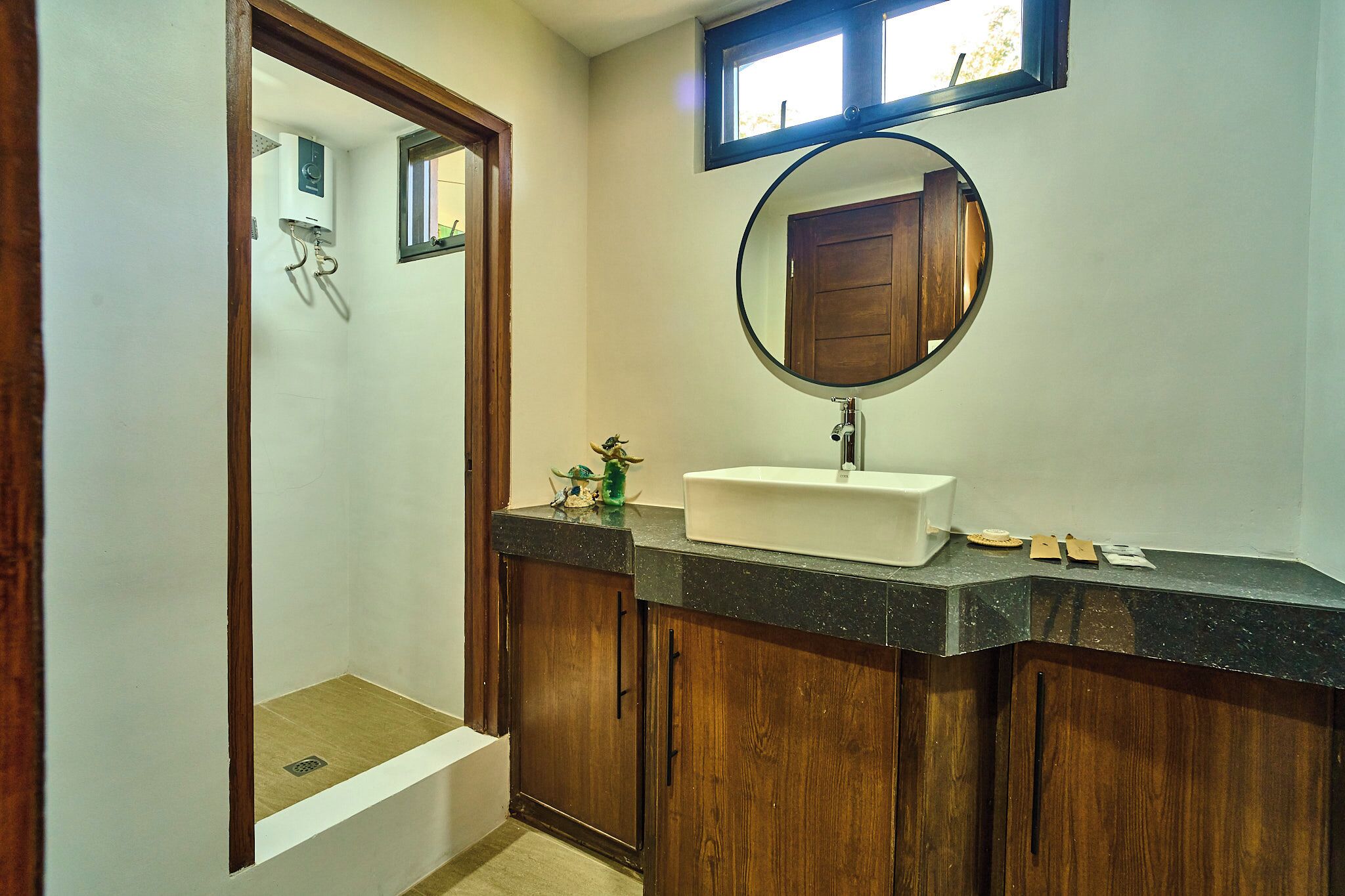 Une salle de bain avec un meuble-lavabo en bois, un miroir rond et un lavabo blanc.