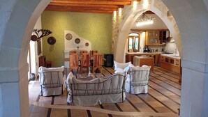 A dining area with a round table and chairs, a kitchen in the background, and an arched ceiling.