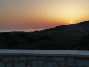 A sunset over a hilly landscape with a stone wall in the foreground.
