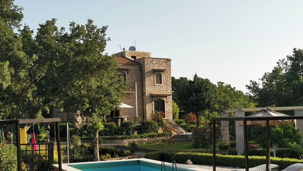 A stone building with a swimming pool, outdoor seating, and a garden.