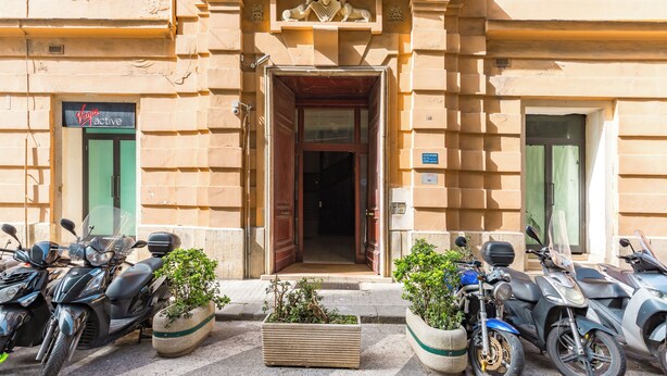A building entrance with a double door, a sign for 'Virgin Active', and several parked motorcycles. - Santa Lucia Seaview (Naples)