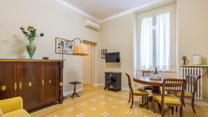 A dining area with a wooden table, chairs, and a vase of flowers on a cabinet. - Santa Lucia Seaview (Naples)