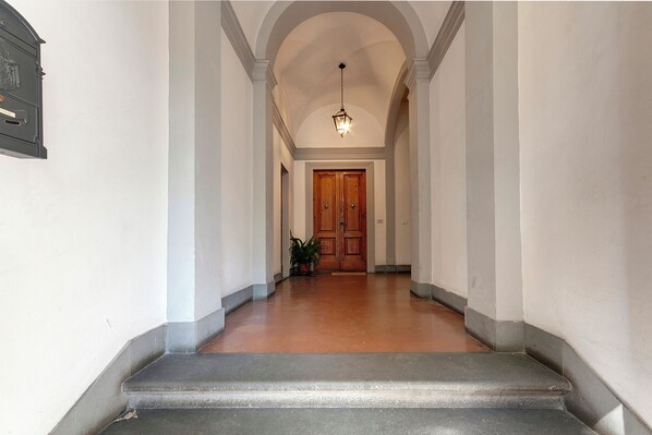 A hallway with a wooden door at the end, a potted plant, and a light fixture on the ceiling.