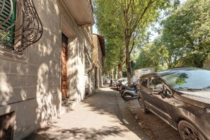 Une rue étroite bordée de voitures garées et d’arbres, avec des immeubles de chaque côté.