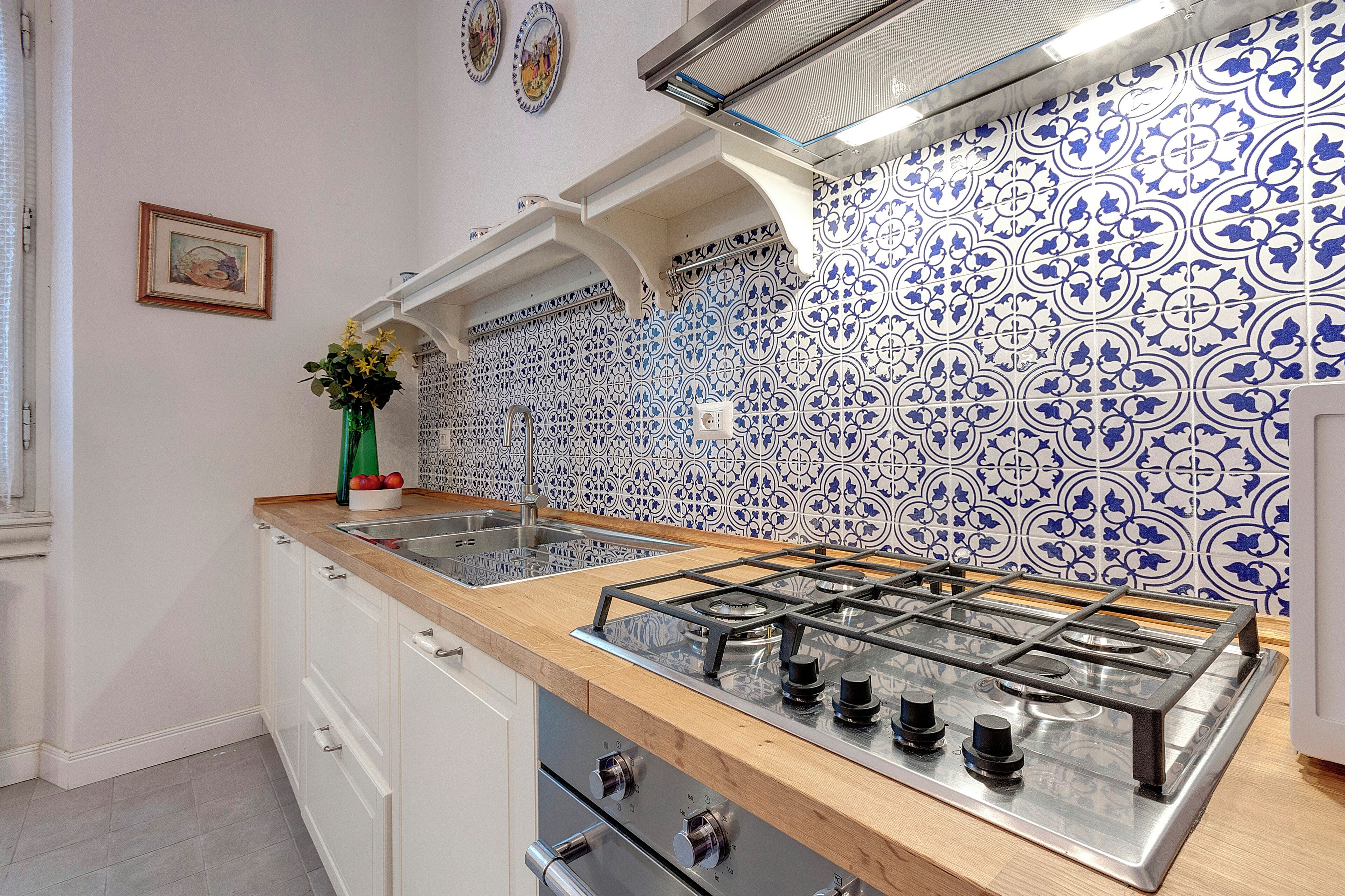 A kitchen with a gas stove, white cabinets, and blue and white patterned tiles.