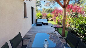 An outdoor patio with a wooden pergola, a glass table with chairs, and a view of a garden with red flowers and green shrubs. - Villa Lillecorsa in porto vecchio (Lecci)