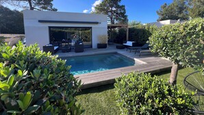 A modern outdoor pool area with a wooden deck, lounge seating, and a covered patio. - Villa Lillecorsa in porto vecchio (Lecci)