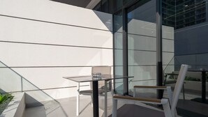 Ein moderner Außenbereich mit Glastisch und Metallstühlen, neben einem Gebäude mit großen Fenstern.