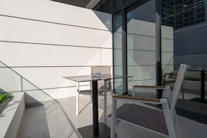 A modern outdoor seating area with a glass table and metal chairs, adjacent to a building with large windows. - Trendy Loft Studio in Oxford Terrace JVC (Dubai)