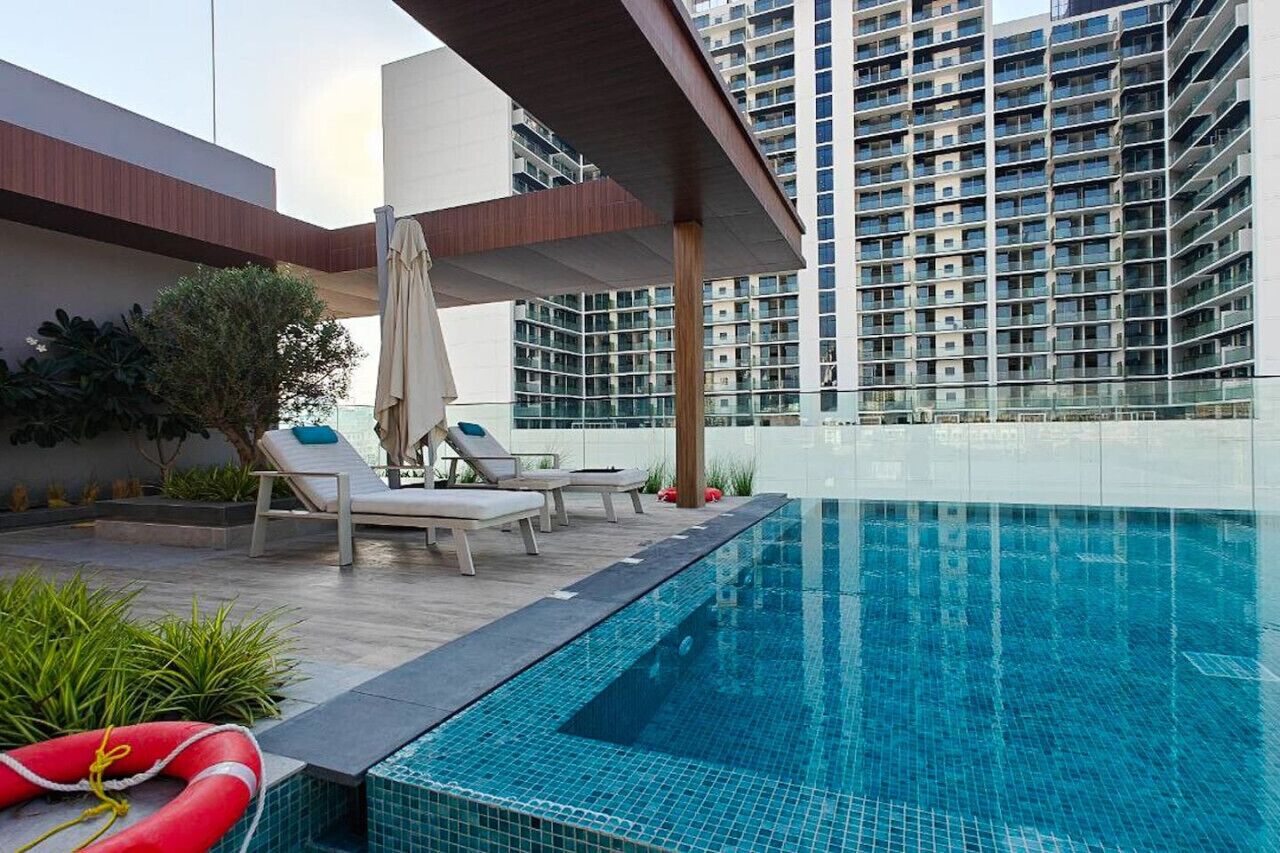 Un espace piscine aménagé sur le toit, avec des chaises longues et une bouée de sauvetage, le tout entouré d’un bâtiment moderne.
