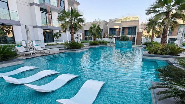 Ein moderner Hotelpoolbereich mit klarem, blauem Wasser, weißen Liegestühlen und Palmen.