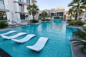 Zona de piscina moderna de hotel con agua azul cristalina, sillones blancos y palmeras.