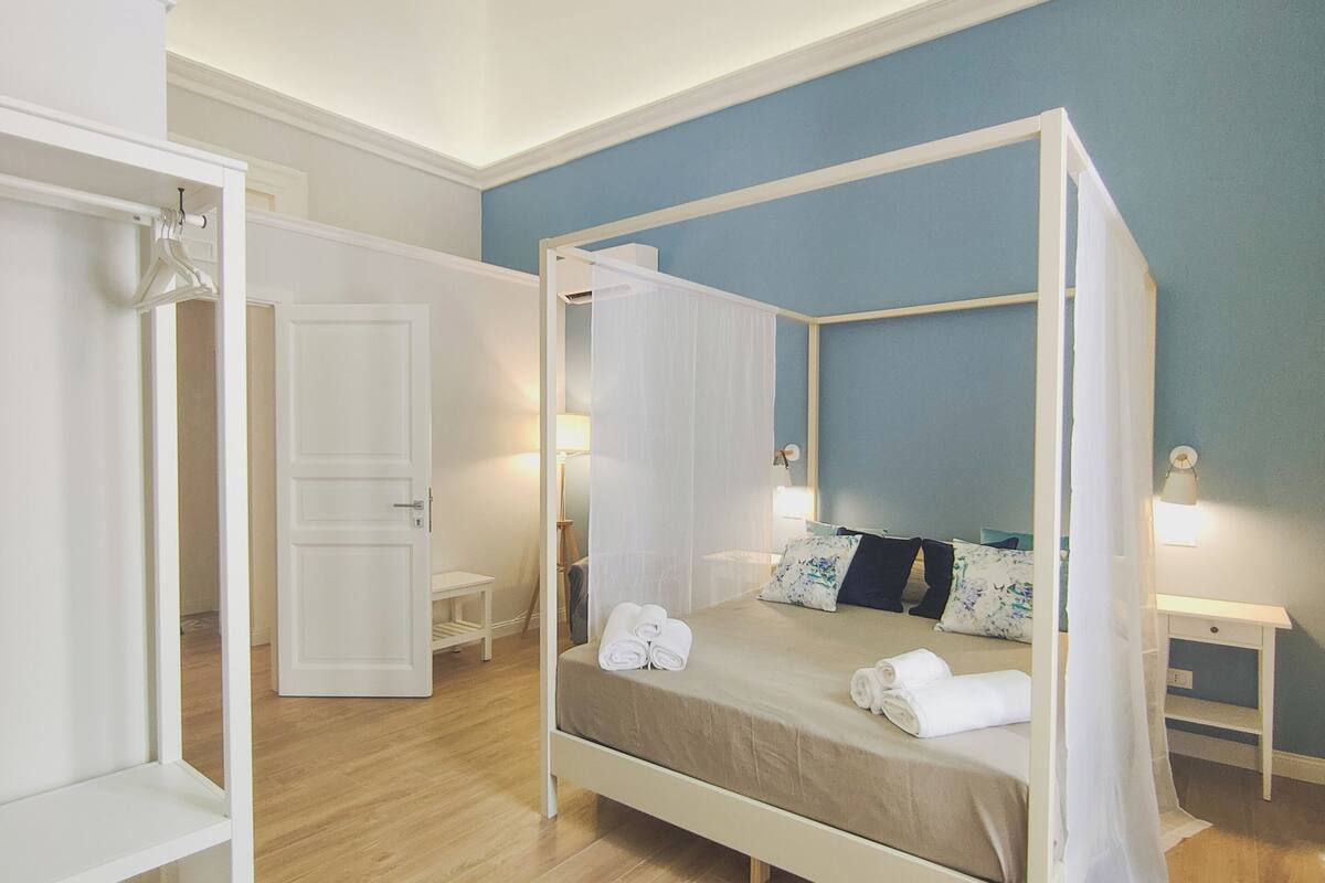 Um quarto com uma cama de dossel, um guarda-roupa, uma mesa de cabeceira e uma mesinha de apoio.
