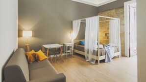 A modern bedroom with a grey sofa, a small table, a bedside table, a bed with a canopy, and a stone wall. - Dimora Carella (Palermo)