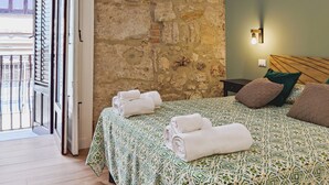 A bedroom with a stone wall, a bed with patterned bedding, a nightstand, and a balcony view. - Dimora Carella (Palermo)
