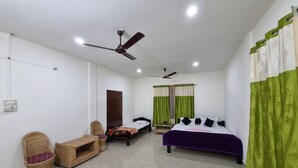 A bedroom with a bed, two chairs, a small table, and two ceiling fans. - Akash Deep Bhawan By GRB (Bokakhat)