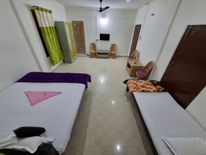 A hotel room with two beds, a television, a ceiling fan, and a small seating area with a chair and a table.