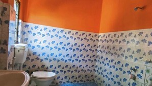 A bathroom with orange walls, a toilet, a sink, and a blue bucket. - Akash Deep Bhawan By GRB (Bokakhat)