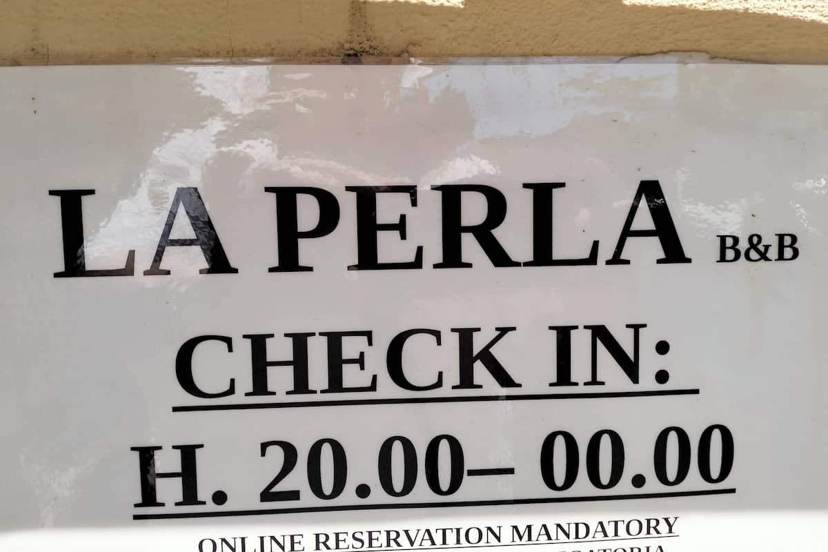 Ein Hotelschild mit dem Namen 'LA PERLA B&B' und der Angabe 'Einchecken 20:00-00:00'.