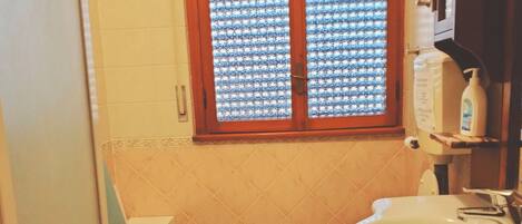Une petite salle de bain avec des toilettes, un lavabo et une baignoire. Il y a une fenêtre avec un rideau à motifs.