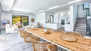 A spacious living area with a large wooden dining table, wicker chairs, and a modern kitchen in the background. - Marbella Holiday Villa with Sea Views & Heated Pool, Gym (AN)
