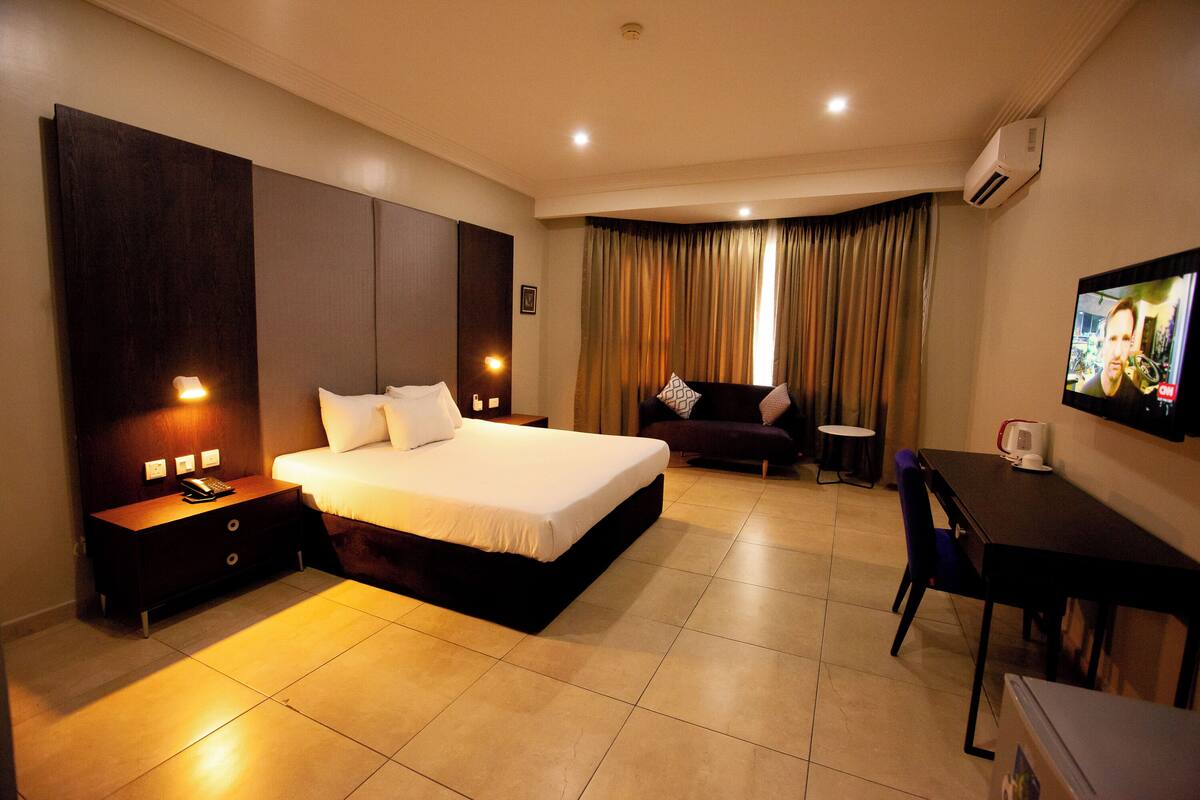 A hotel room with a large bed, bedside tables, a desk, a chair, a TV, and a window with curtains.