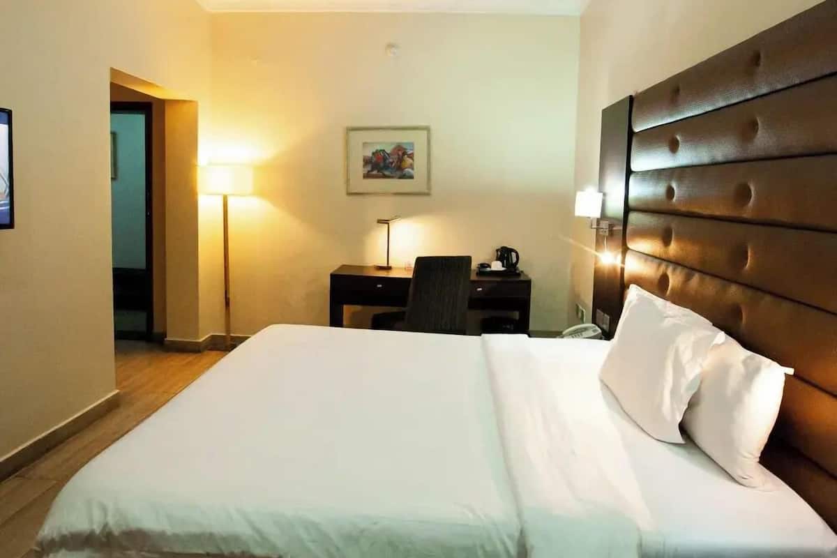 A hotel room with a large bed, a desk, a chair, a lamp, and a painting on the wall.