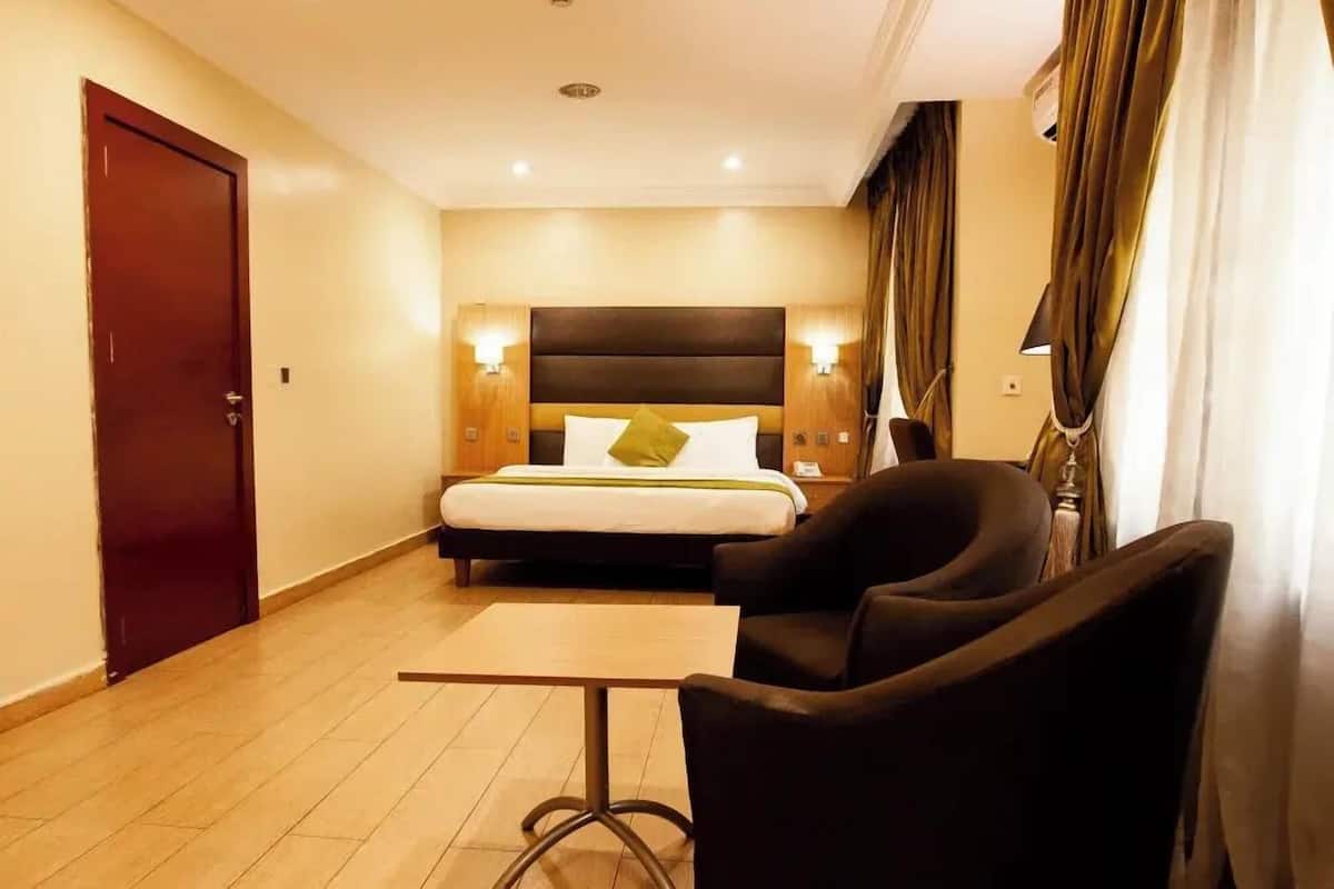 A hotel room with a bed, a desk, a chair, and a door.