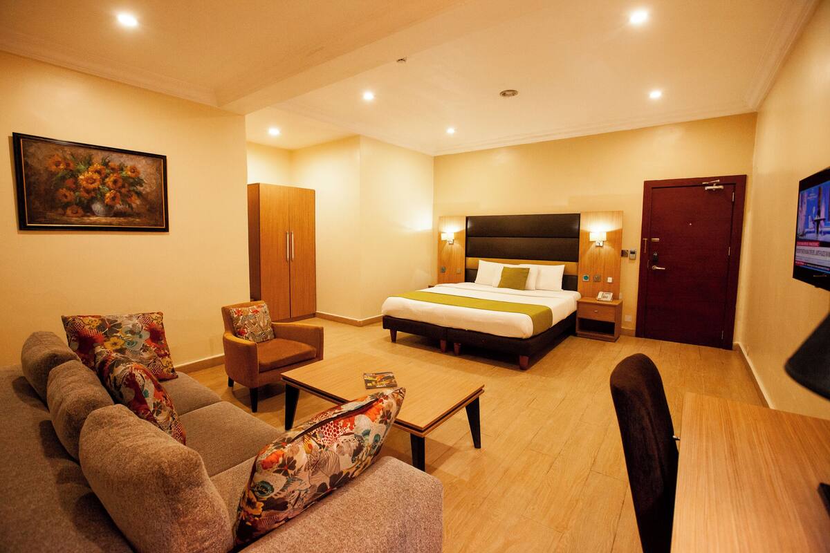 A hotel room with a bed, sofa, armchair, and a television.