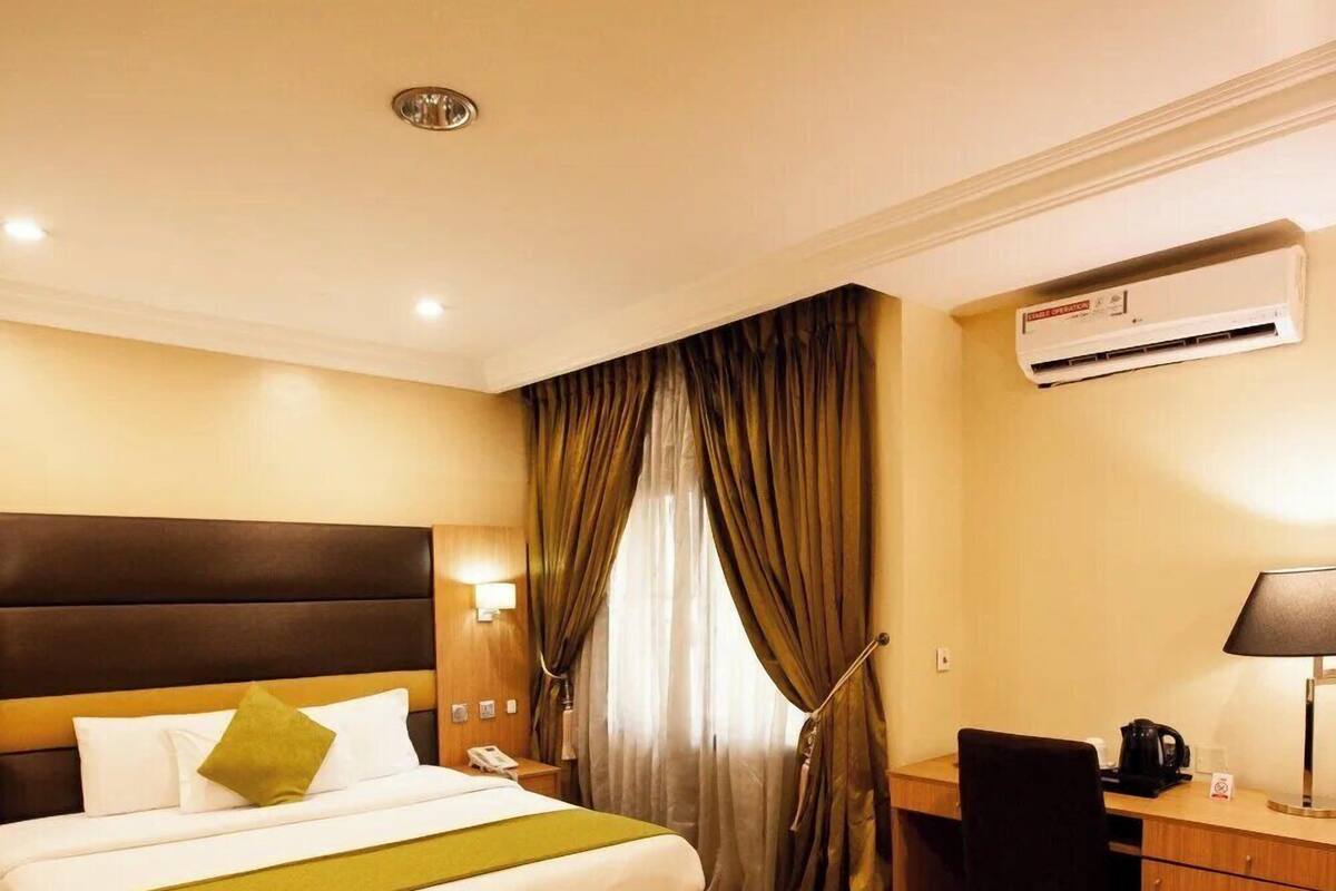 A hotel room with a bed, desk, chair, and an air conditioning unit.