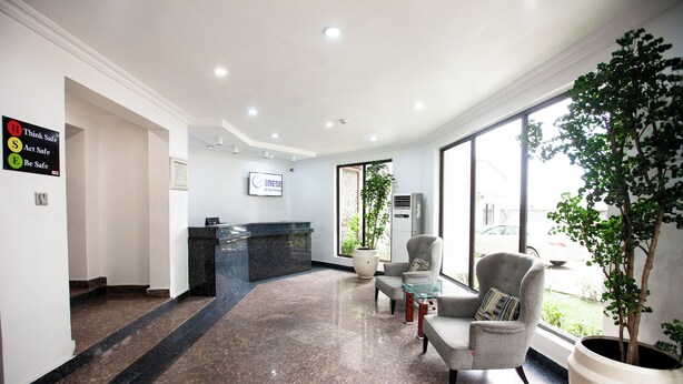 A reception area with a marble floor, a reception desk, two armchairs, a large potted plant, and a sign with safety instructions. - Genesis Castle (Port Harcourt)