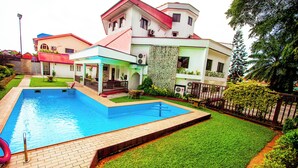 A swimming pool surrounded by a well-maintained lawn, a patio with outdoor furniture, and a multi-story building with balconies. - Genesis Castle (Port Harcourt)