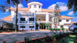 A modern two-story building with a central entrance, surrounded by a landscaped garden and a parked car. - Genesis Castle (Port Harcourt)
