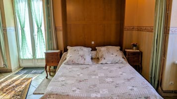 Une chambre à coucher avec un grand lit, deux tables de chevet, une tête de lit en bois, une fenêtre avec des rideaux et un tapis à motifs.