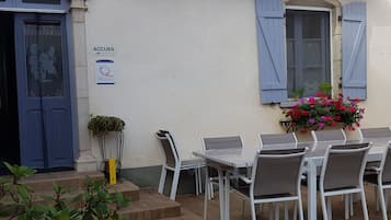 Un espace extérieur aménagé avec des tables et des chaises blanches, une porte bleue et une enseigne indiquant « ACCUEIL ».