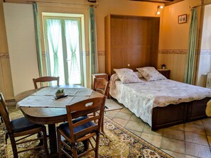 A room with a bed, a table with chairs, a window with curtains, and a wooden wardrobe.